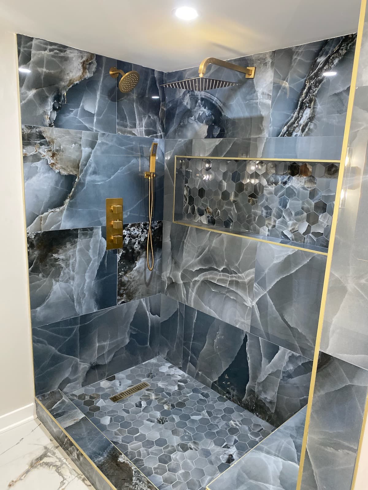 Walk-in shower with dark marble tile and gold fixtures